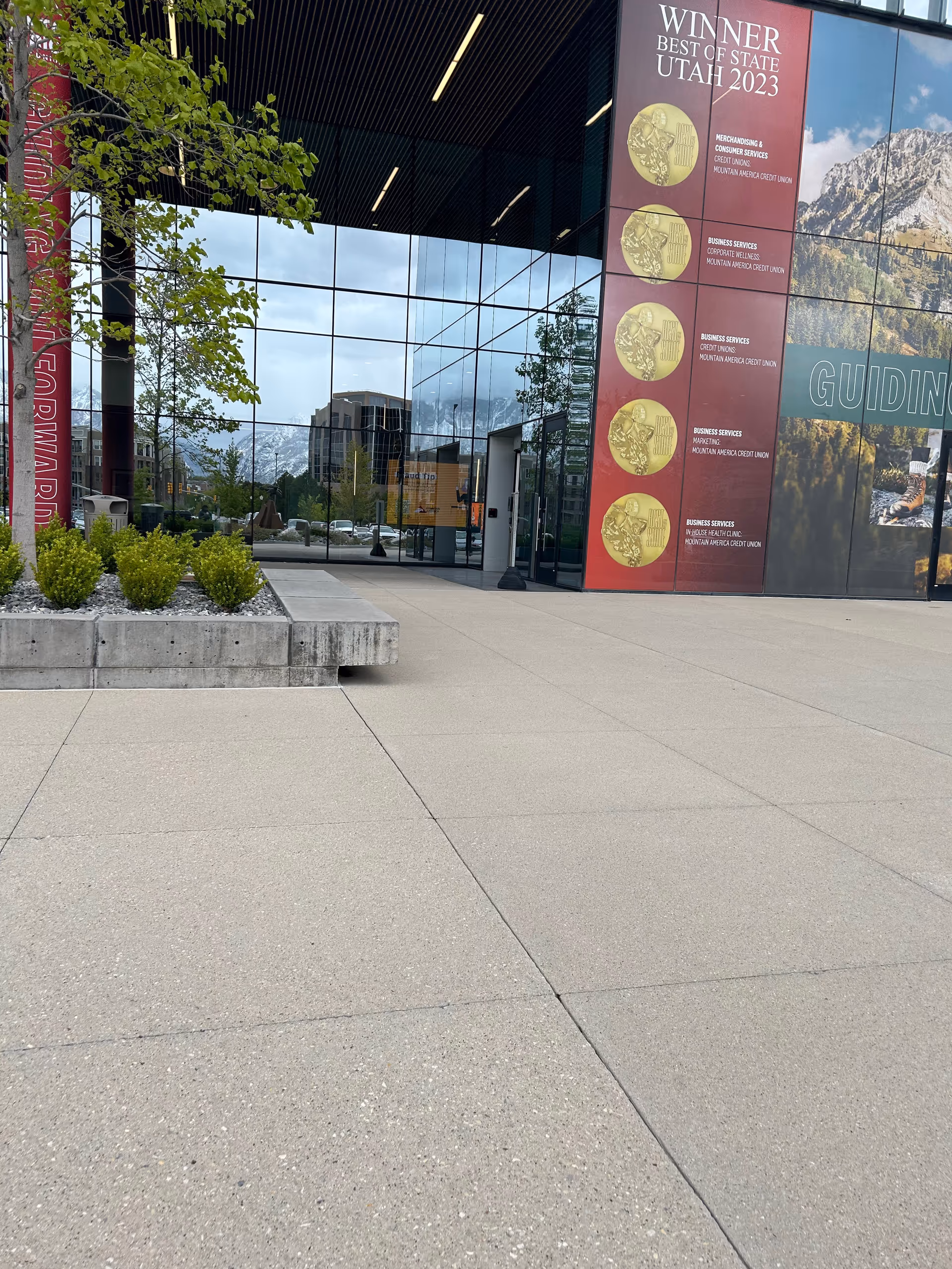 Modern glass-front building exterior with banners and a paved plaza.