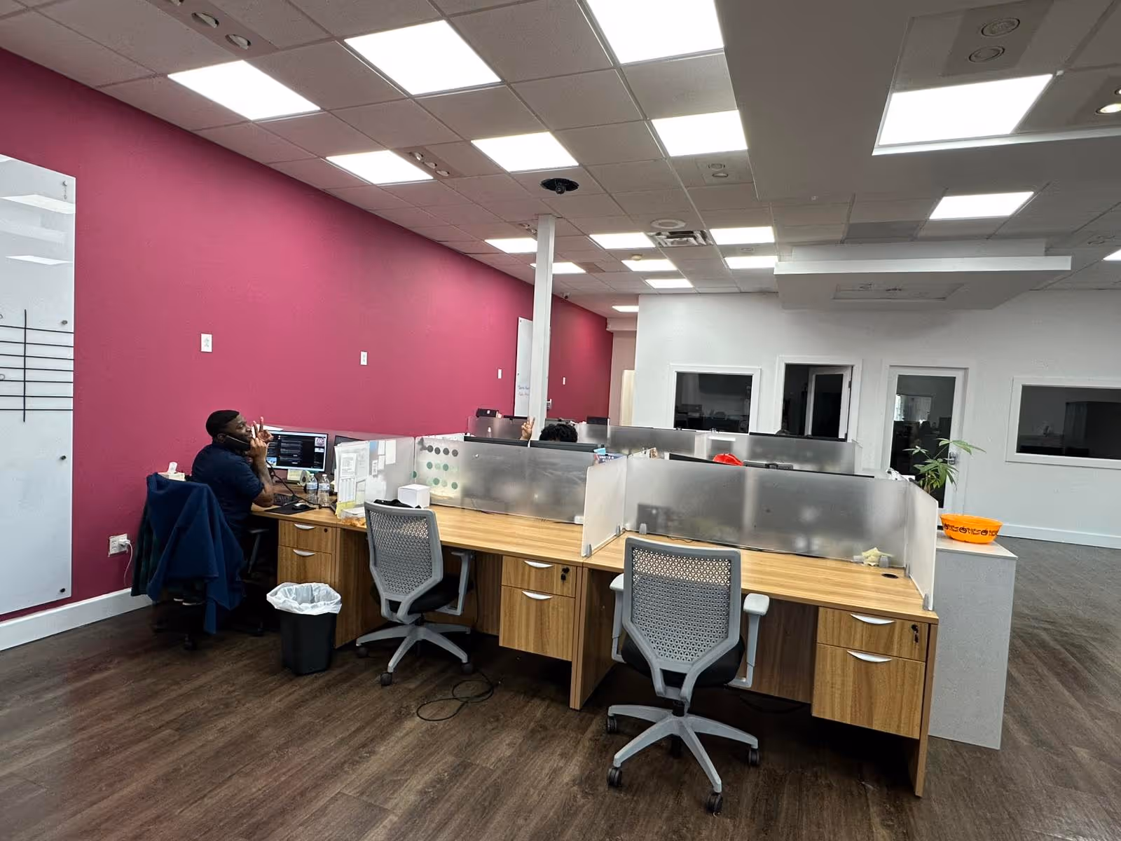 Open office space with cubicles, desks, and a pink accent wall in a senior care facility.
