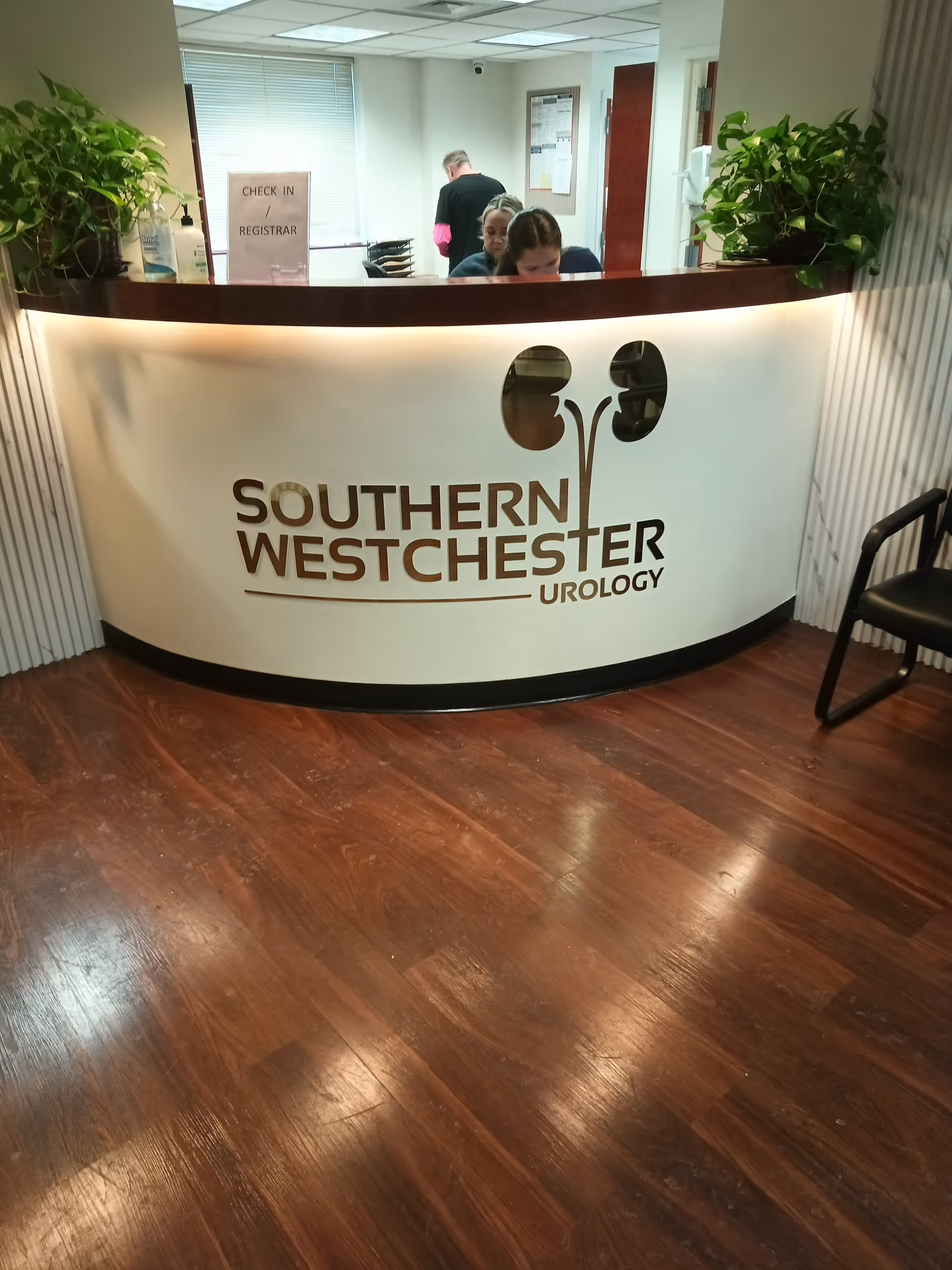 Reception desk with Southern Westchester Urology sign, staff, and plants inside a clinic.