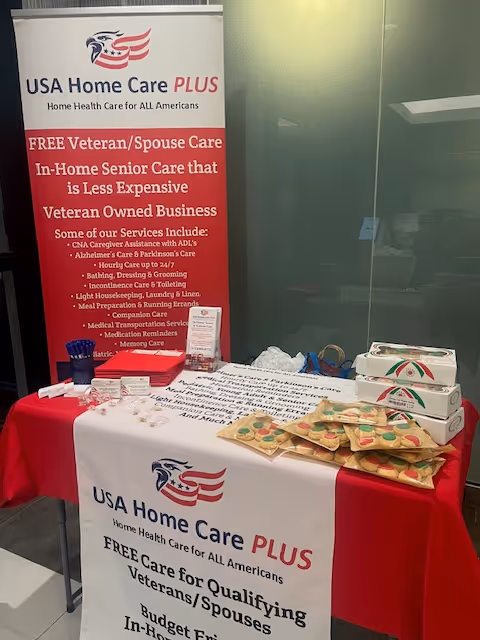 Indoor promotional booth for USA Home Care PLUS with banners and a table of materials.