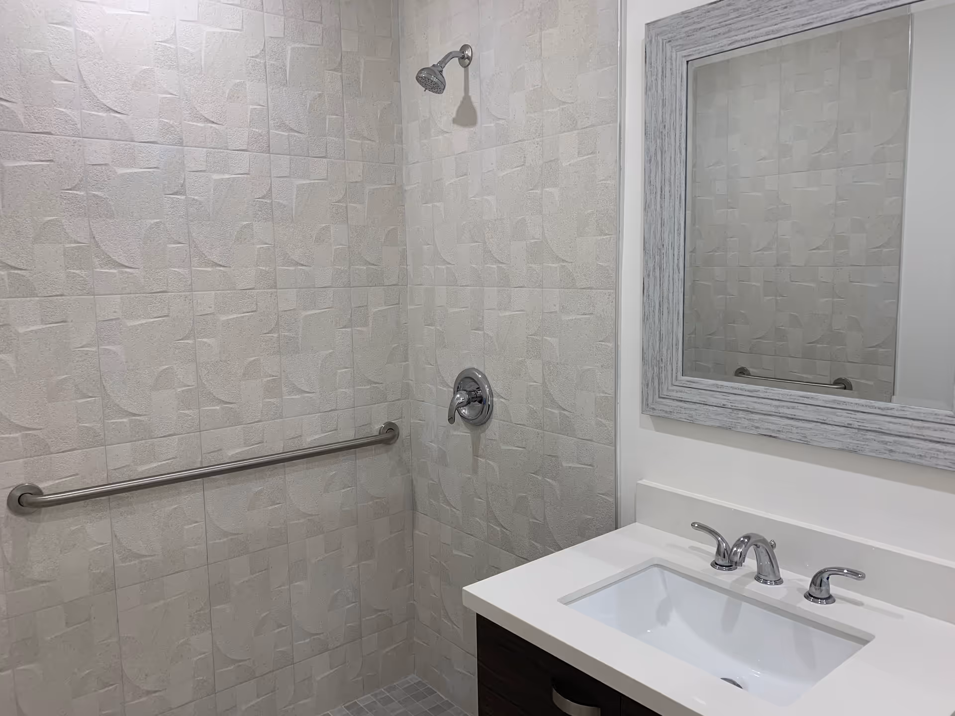 Modern bathroom featuring tiled walk-in shower, grab bar, and sink with mirror.