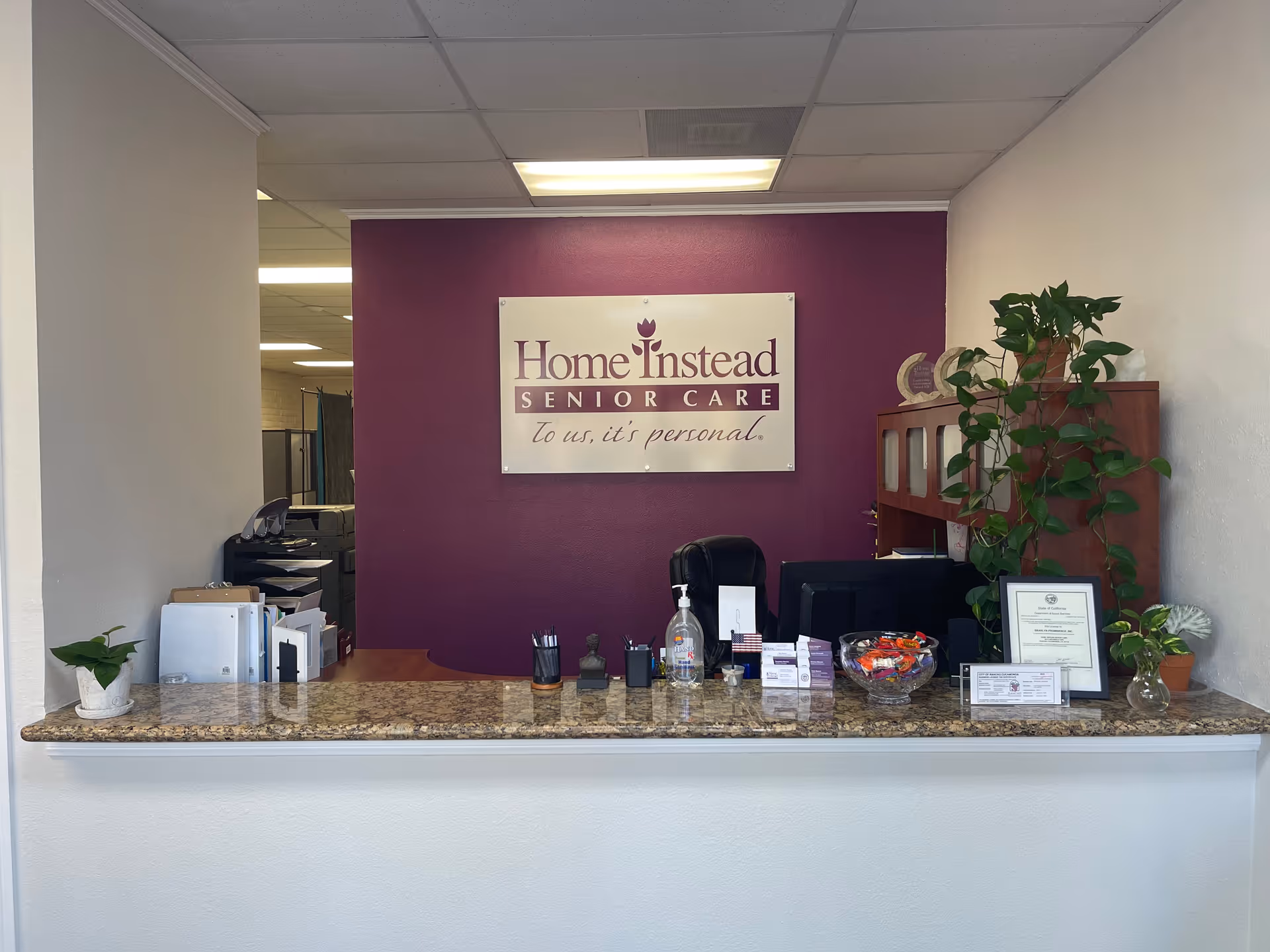 Reception desk in a senior care office with purple backdrop and Home Instead sign.