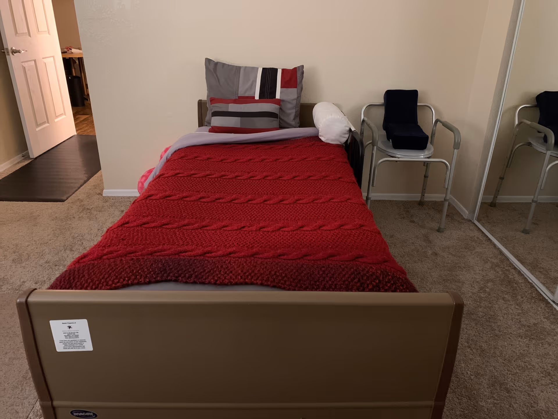 A bedroom with a single bed, red blanket, pillows, and two chairs by the wall.