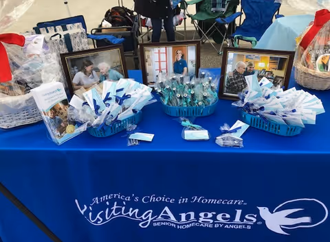 Outdoor event table with blue Visiting Angels branding and several framed photos.