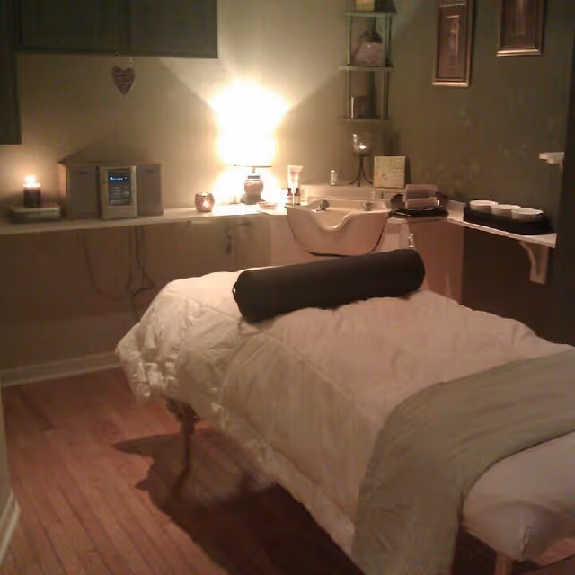 A massage therapy room featuring a massage bed, sink, and warm lighting.