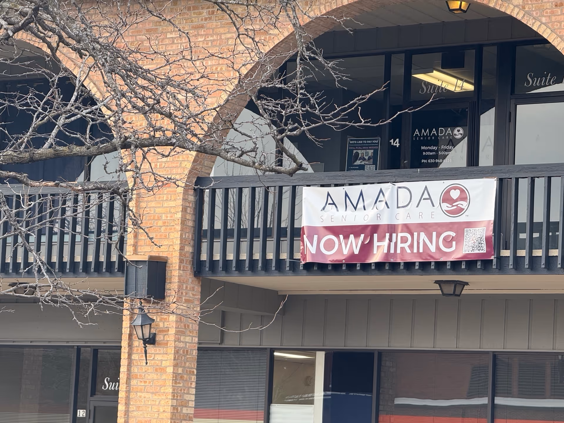 Exterior view of Amada Senior Care building with a Now Hiring banner on the balcony.
