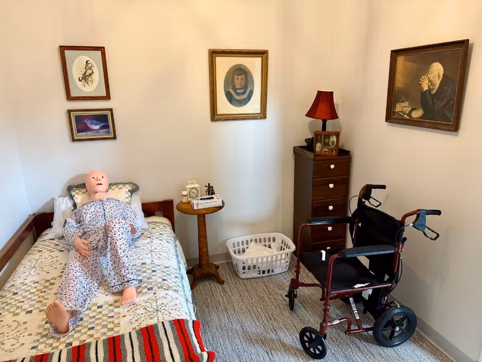 A small bedroom with a bed, walker, dresser, lamp, and framed art.