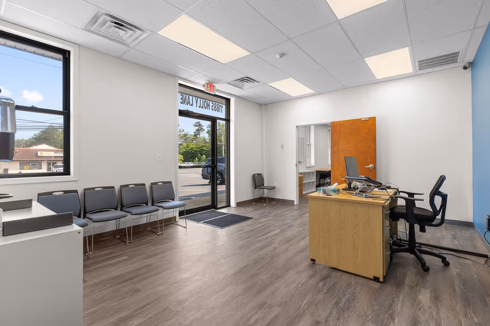 Interior reception area with row chairs, a wooden desk, and a glass entrance.