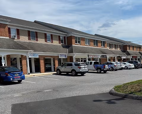 Exterior view of a brick shopping plaza with parked cars in front.
