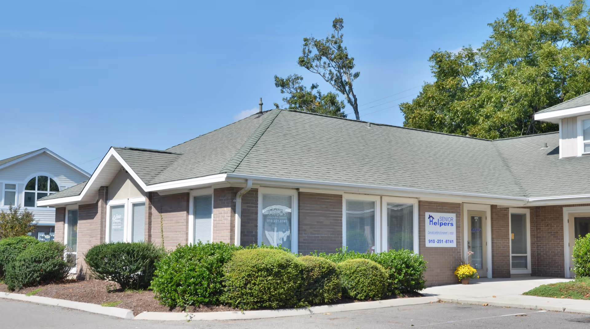 Single-story brick senior living facility exterior with manicured shrubs and a Senior Helpers sign.