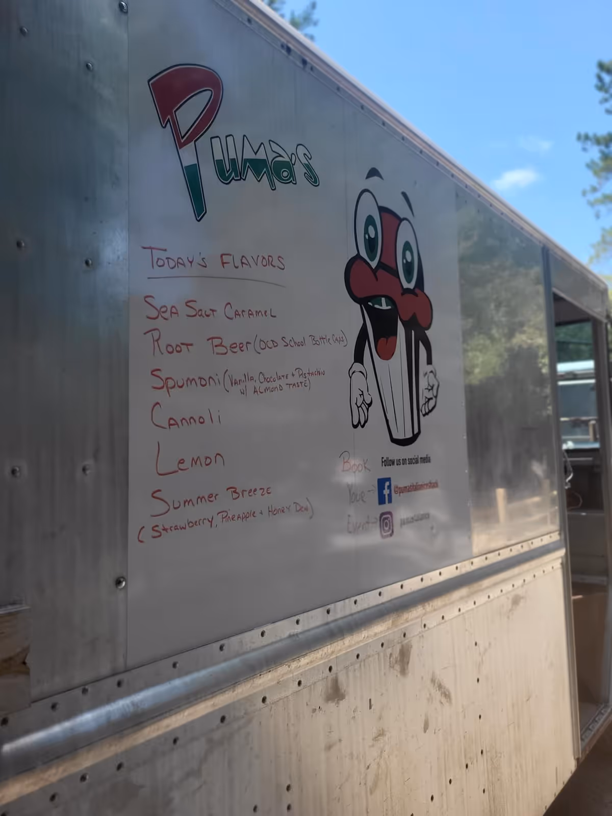 Shiny metal food truck trailer with a cartoon cup character and flavor menu.