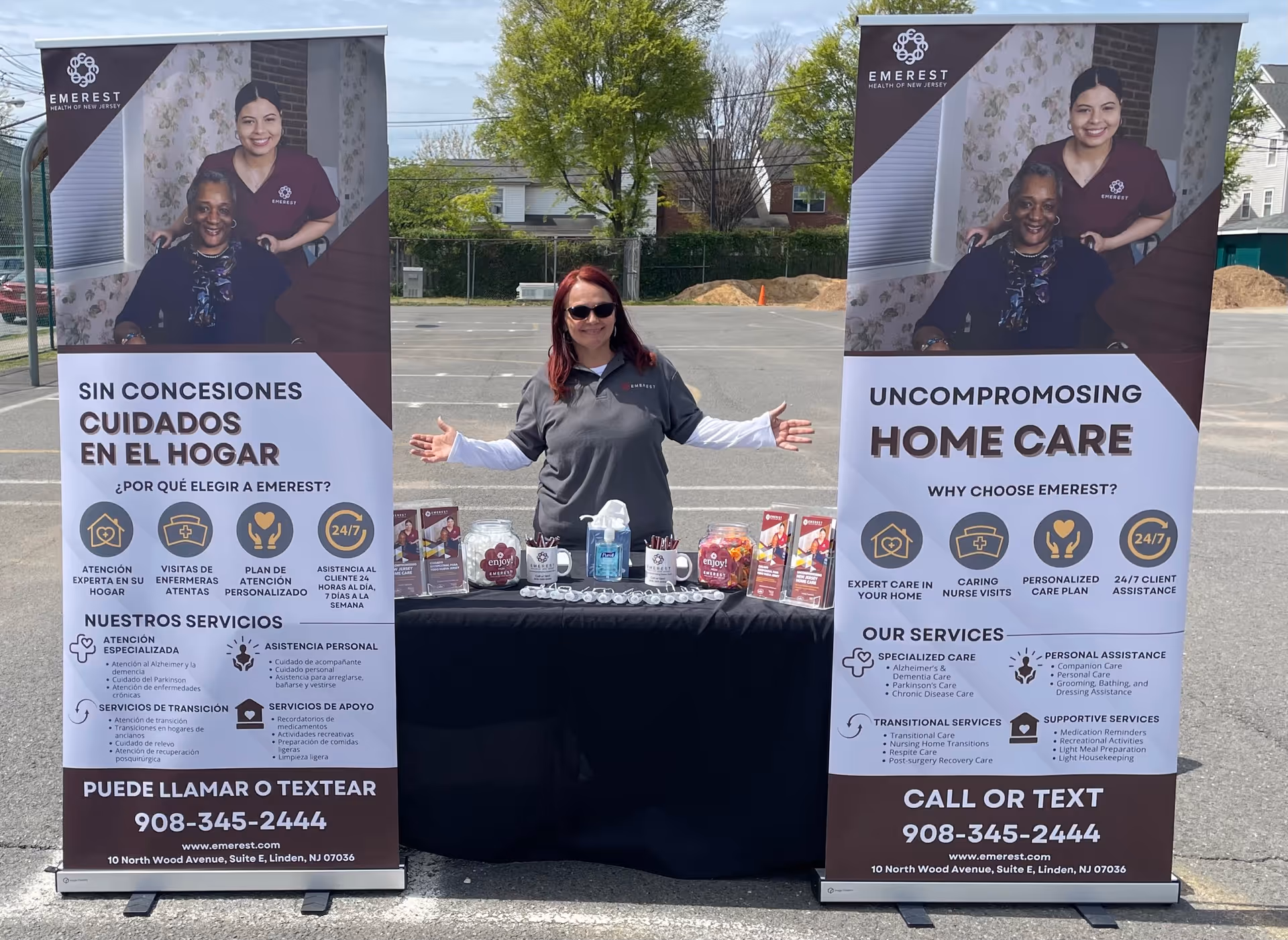 A woman stands behind a table with two tall promotional banners outdoors in a parking lot.