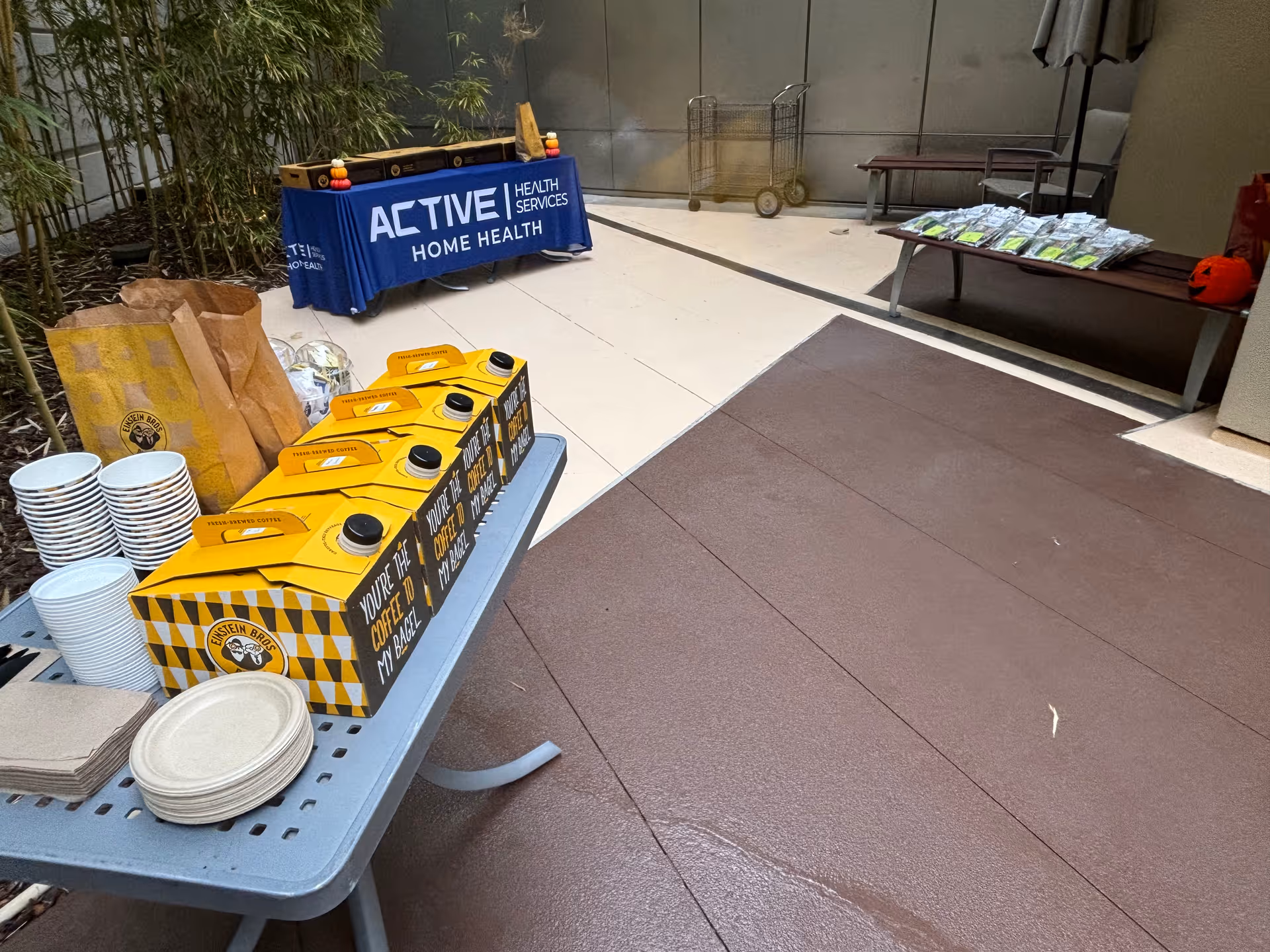 Indoor promotional setup with Active Health Services banner, coffee boxes, cups, and plates.