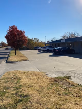 Parking lot with cars and a single-story building beside trees.