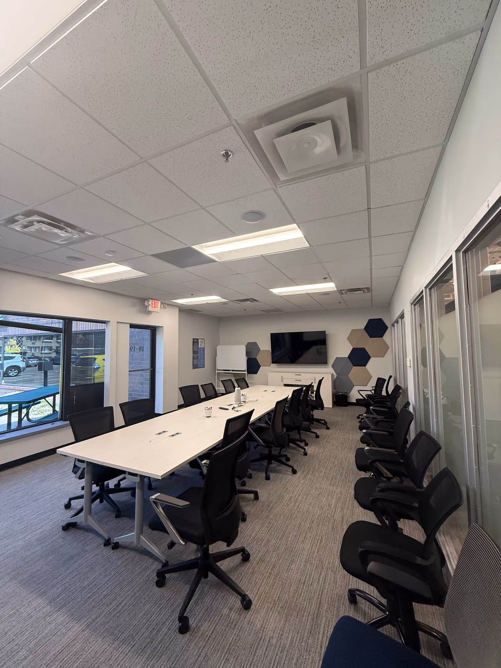 Bright conference room with long table, many chairs, screen, and hexagonal wall decor.