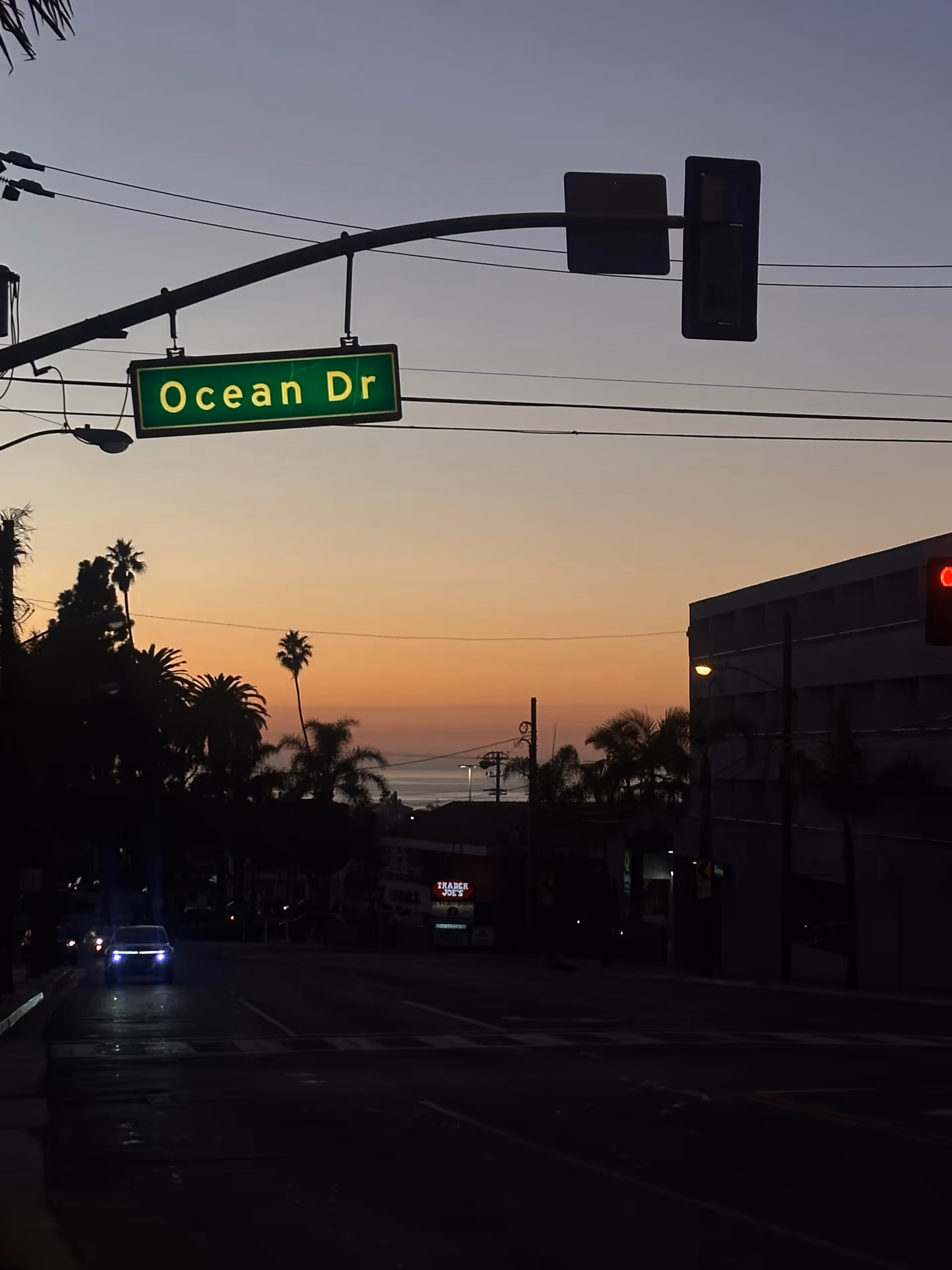 Sunset on Ocean Drive with palm trees, street sign, and silhouetted buildings.