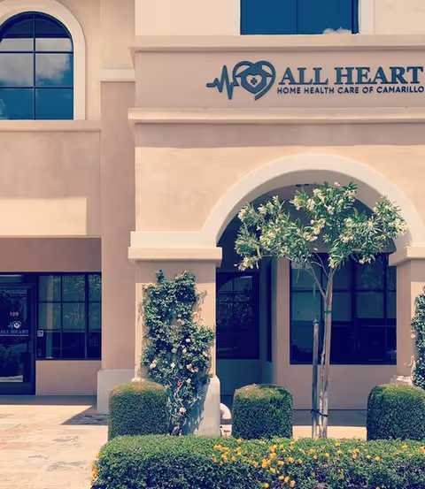 The All Heart Home Health Care sign on a beige building front with arches and landscaping.