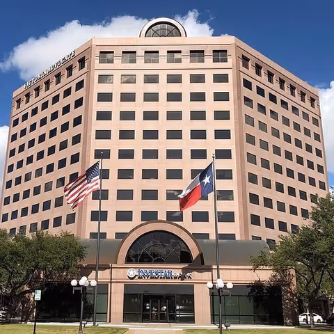 Tall beige office building with flags at the entrance and an arched glass doorway.