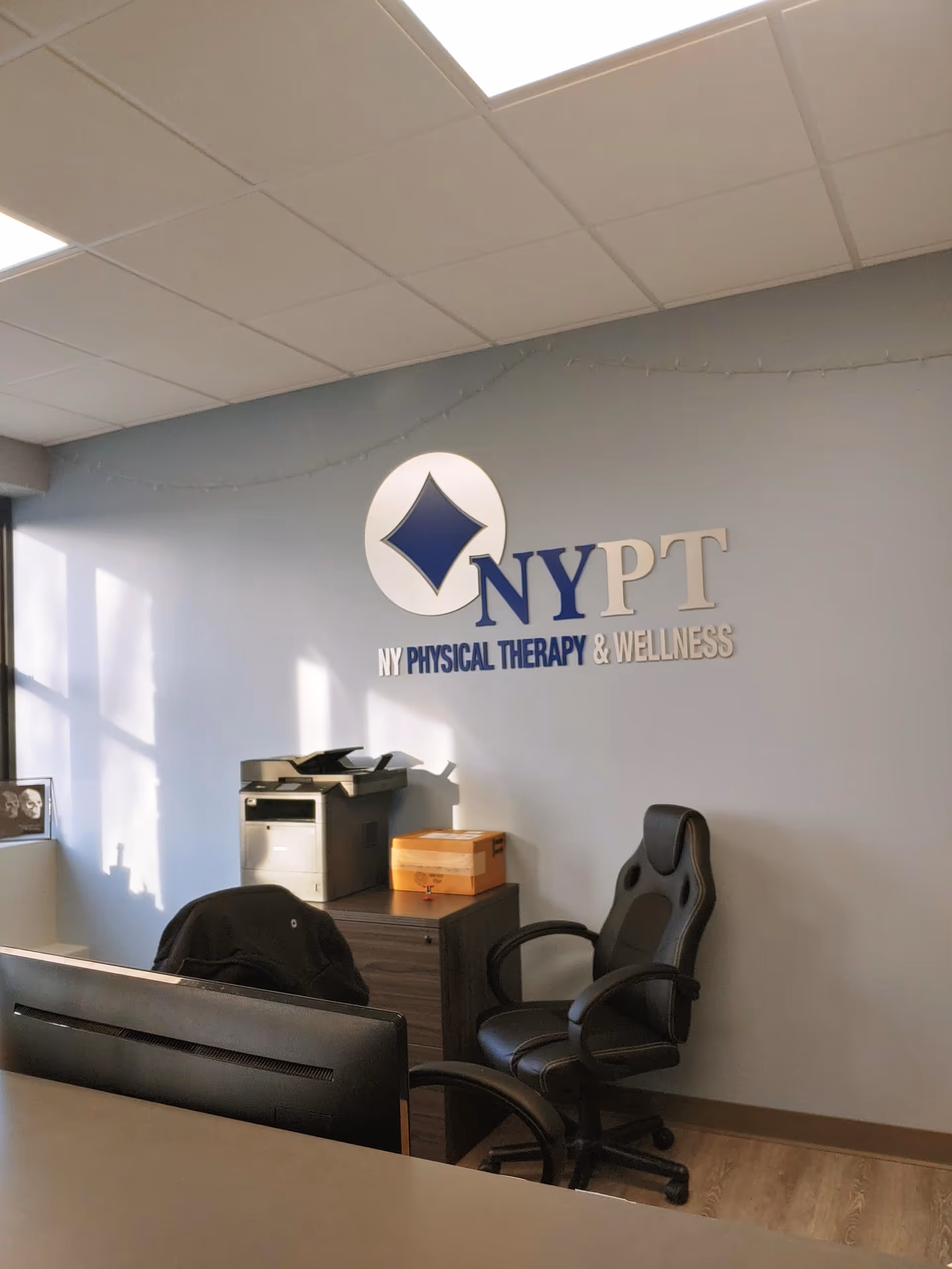 Indoor office area with NYPT logo on wall, desk, chair, printer, and boxes.