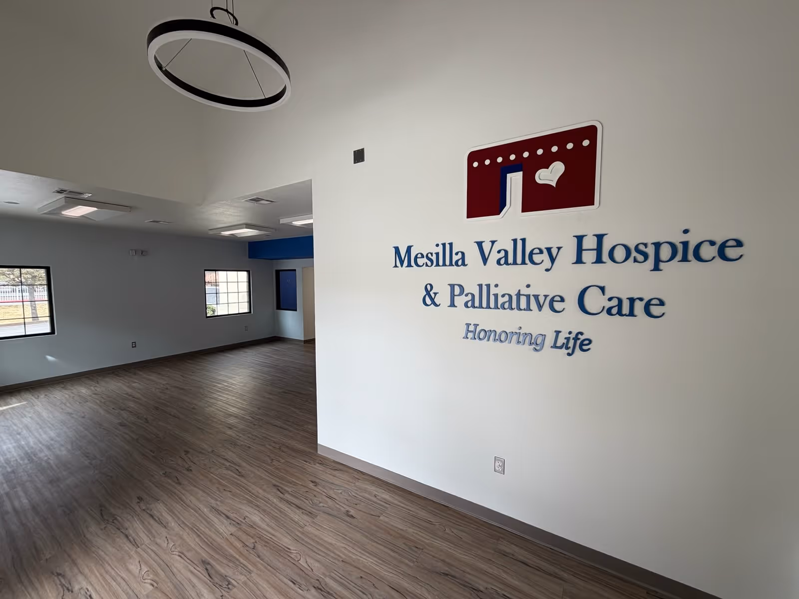 Interior room with wood floors and a white wall displaying Mesilla Valley Hospice sign.