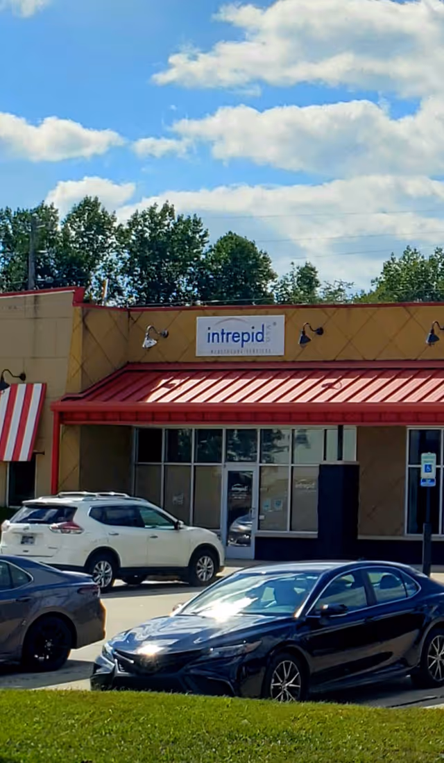 Front view of a beige storefront with an Intrepid sign, red awning, and parked cars.