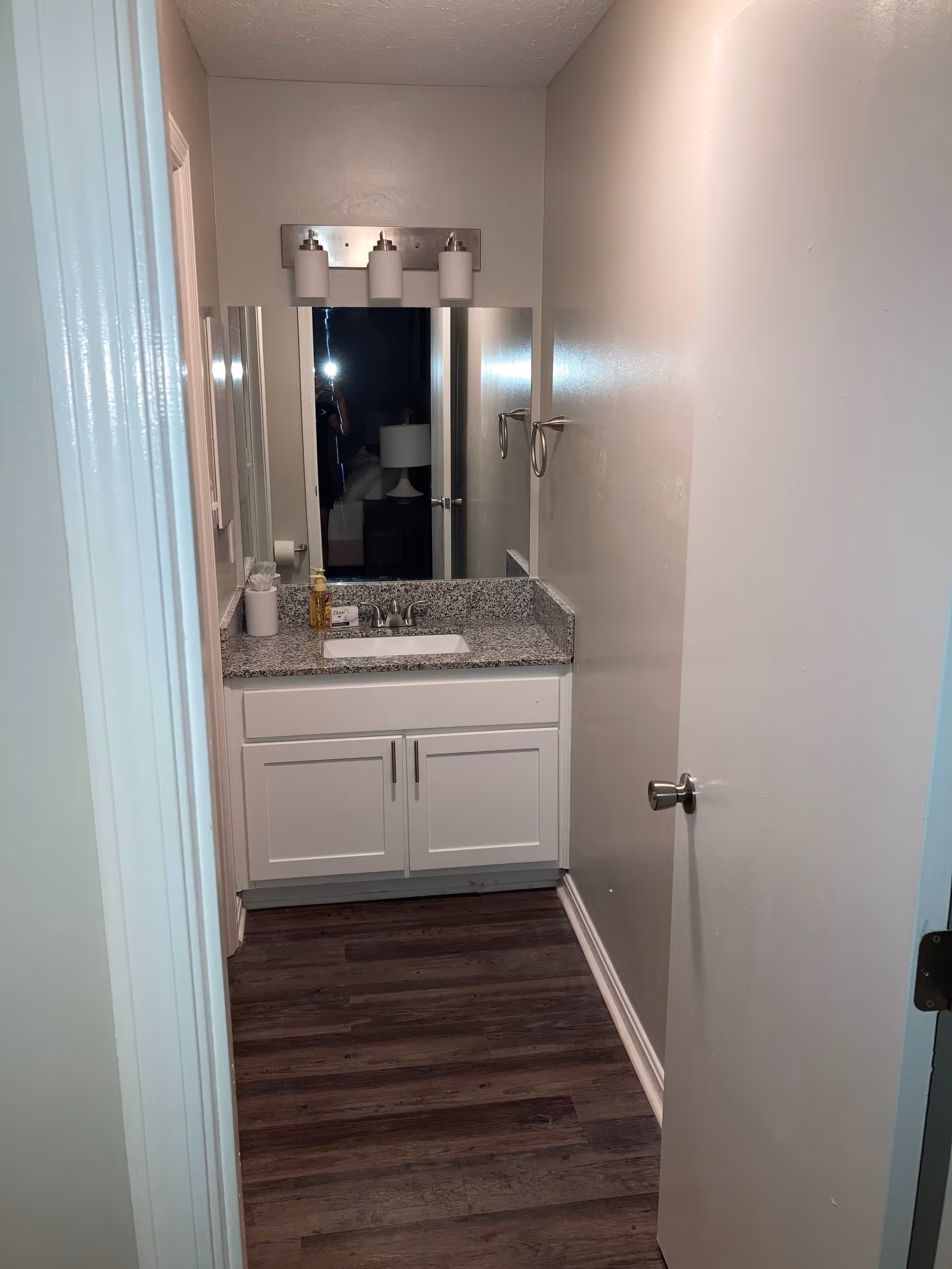 Narrow bathroom with granite countertop sink, mirror, cabinet, and overhead lights.