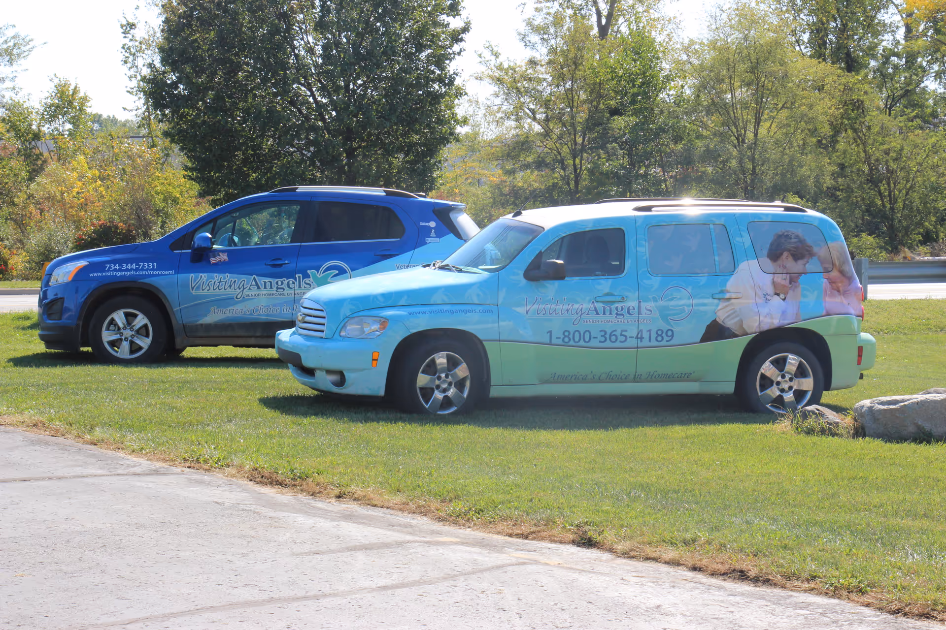 Two Visiting Angels vans parked on a grassy outdoor area.