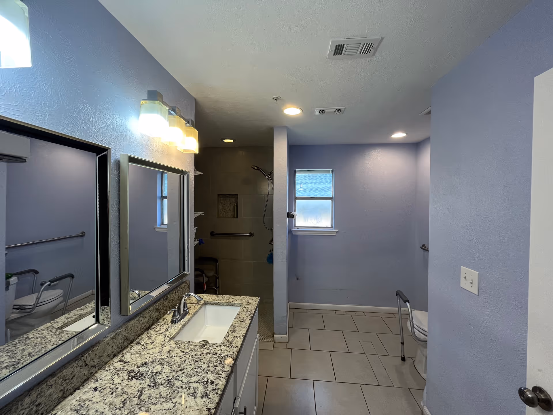 Blue bathroom with granite countertop, double mirrors, sink, and a shower area.