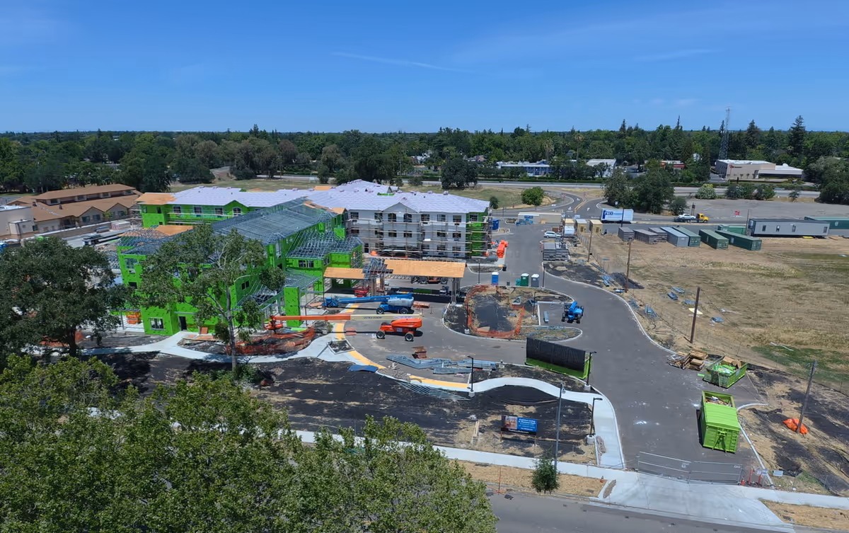 Aerial view of a construction site with bright green building frames and surrounding roads.
