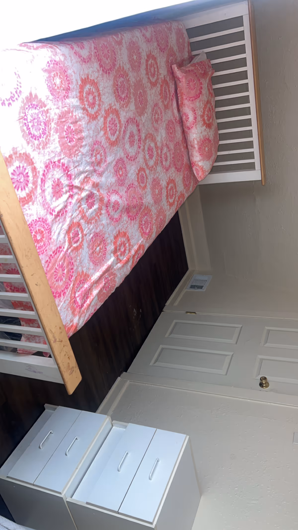 Small bedroom with pink patterned bedding on a white bed frame and dresser.