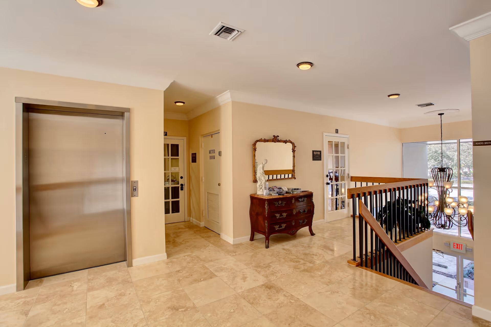 Hallway lobby with elevator, console table, mirror, staircase, and glass doors.