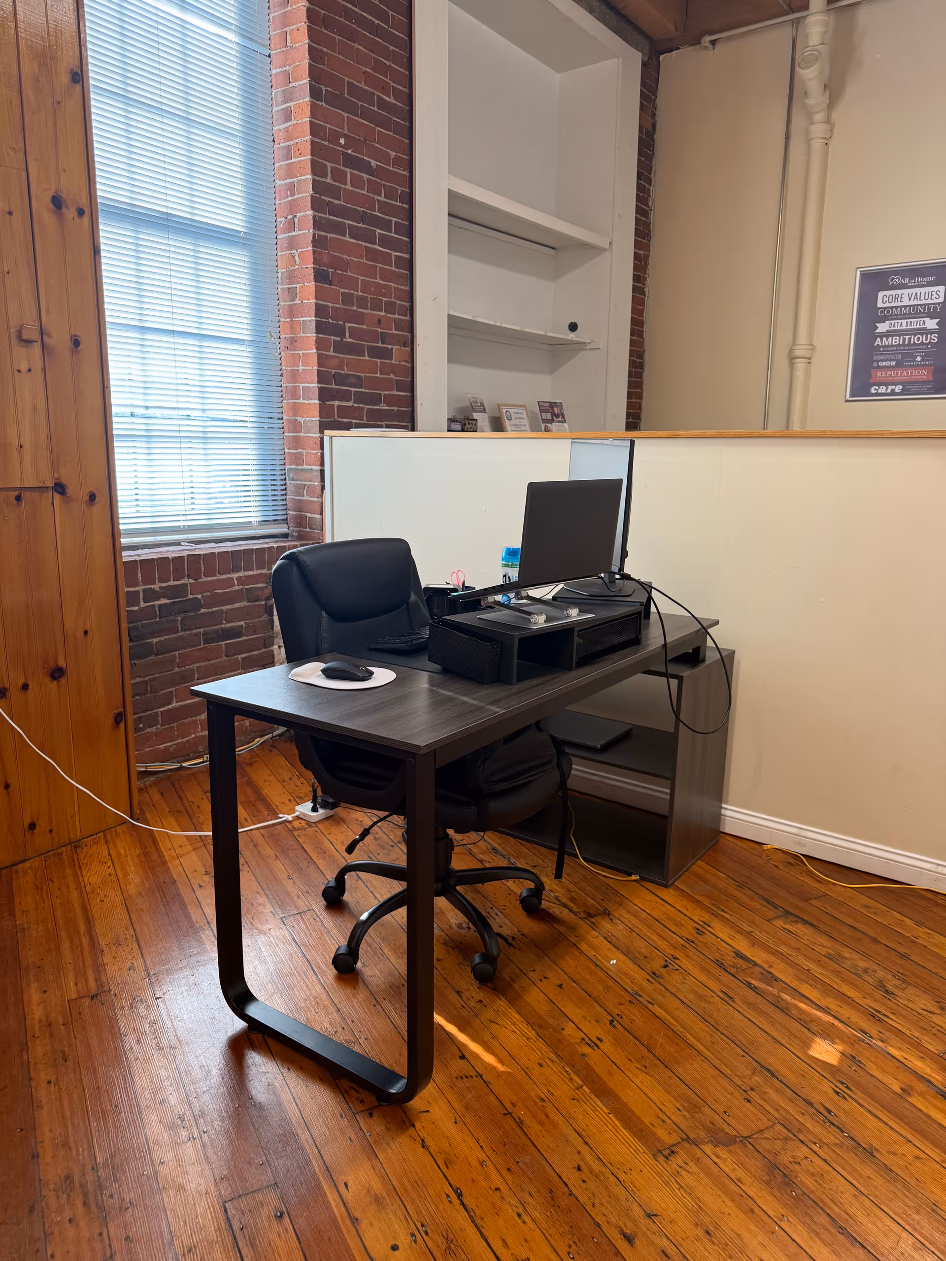 Office desk with computer and chair against brick wall in a small workspace