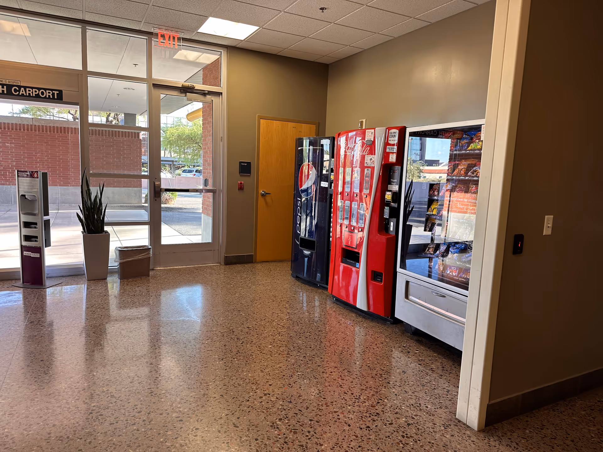 Interior lobby area with vending machines, glass doors, a plant, and terrazzo floor.