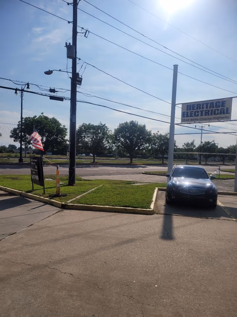 Outdoor parking area with a car, power lines, and a Heritage Electrical sign.