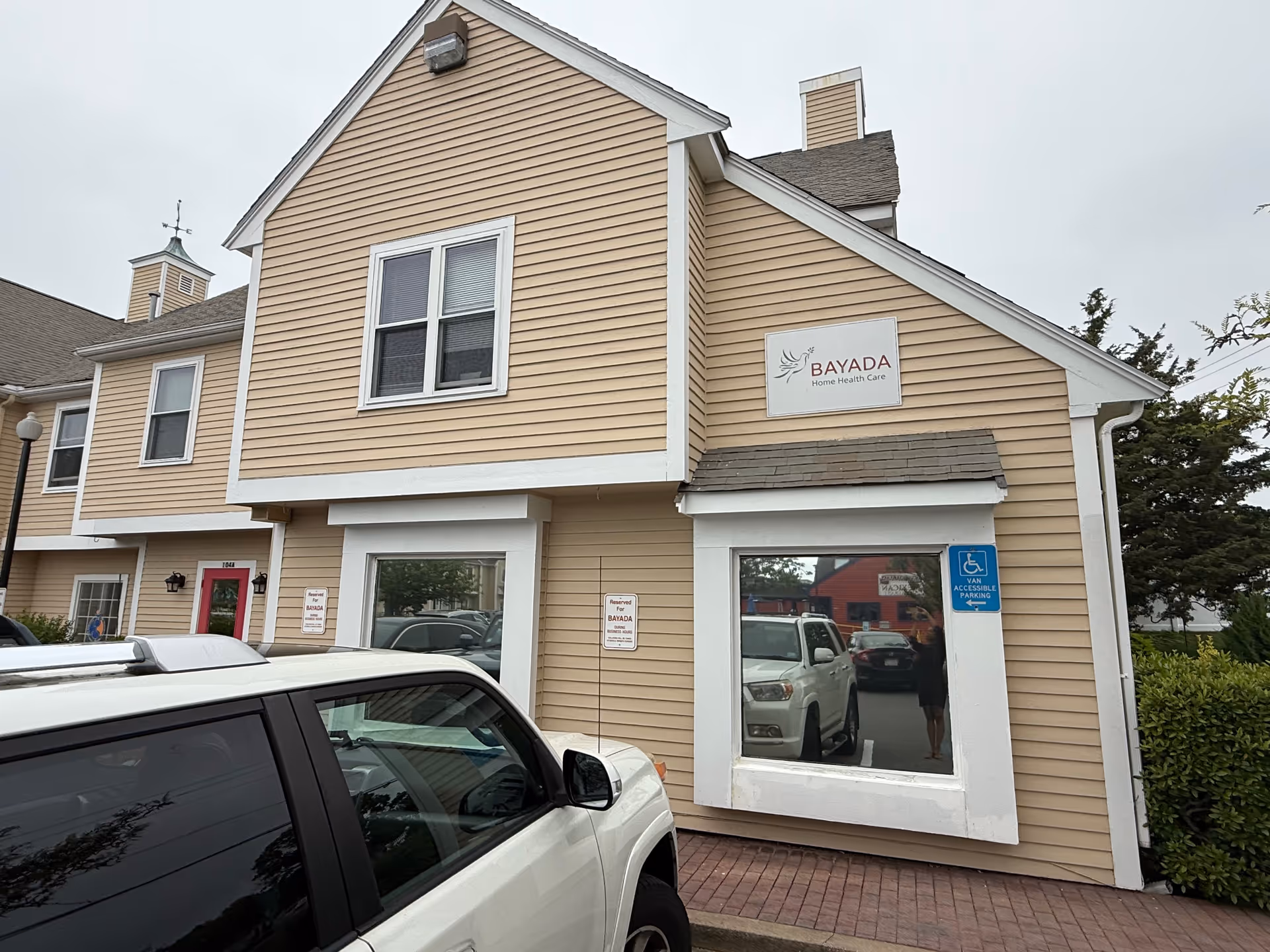 Exterior view of a BAYADA senior care building with beige siding and parked cars.