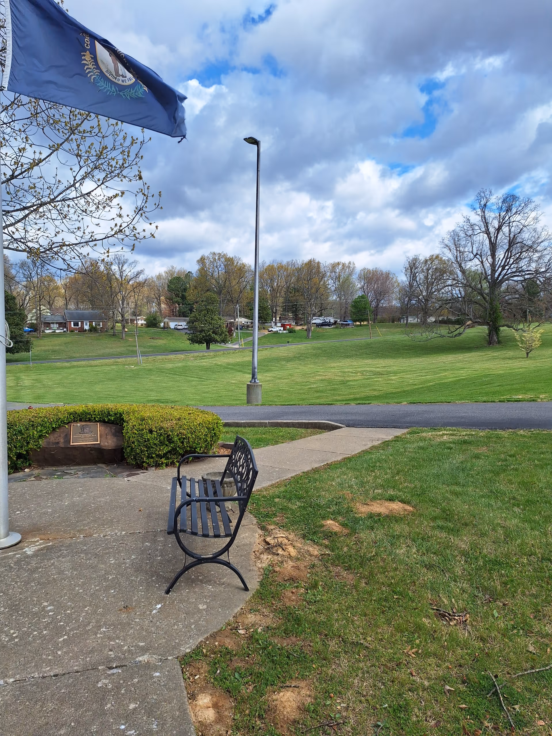 Outdoor plaza at Livingston Hospital with a bench, flag banner, and expansive green lawn.