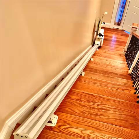A white stairlift track runs along wooden stairs inside a hallway.