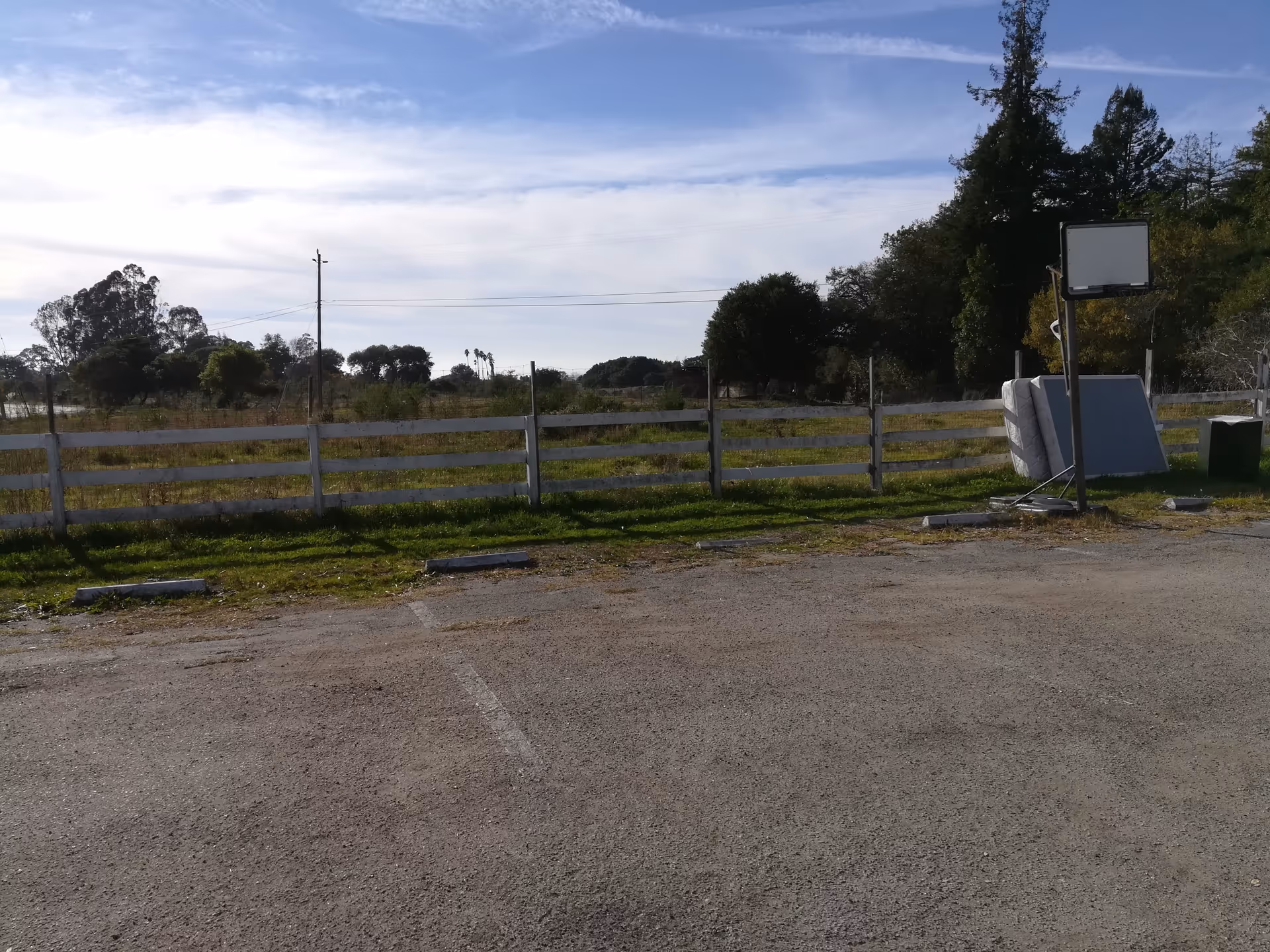 Empty outdoor parking area with a white fence and open field beyond.