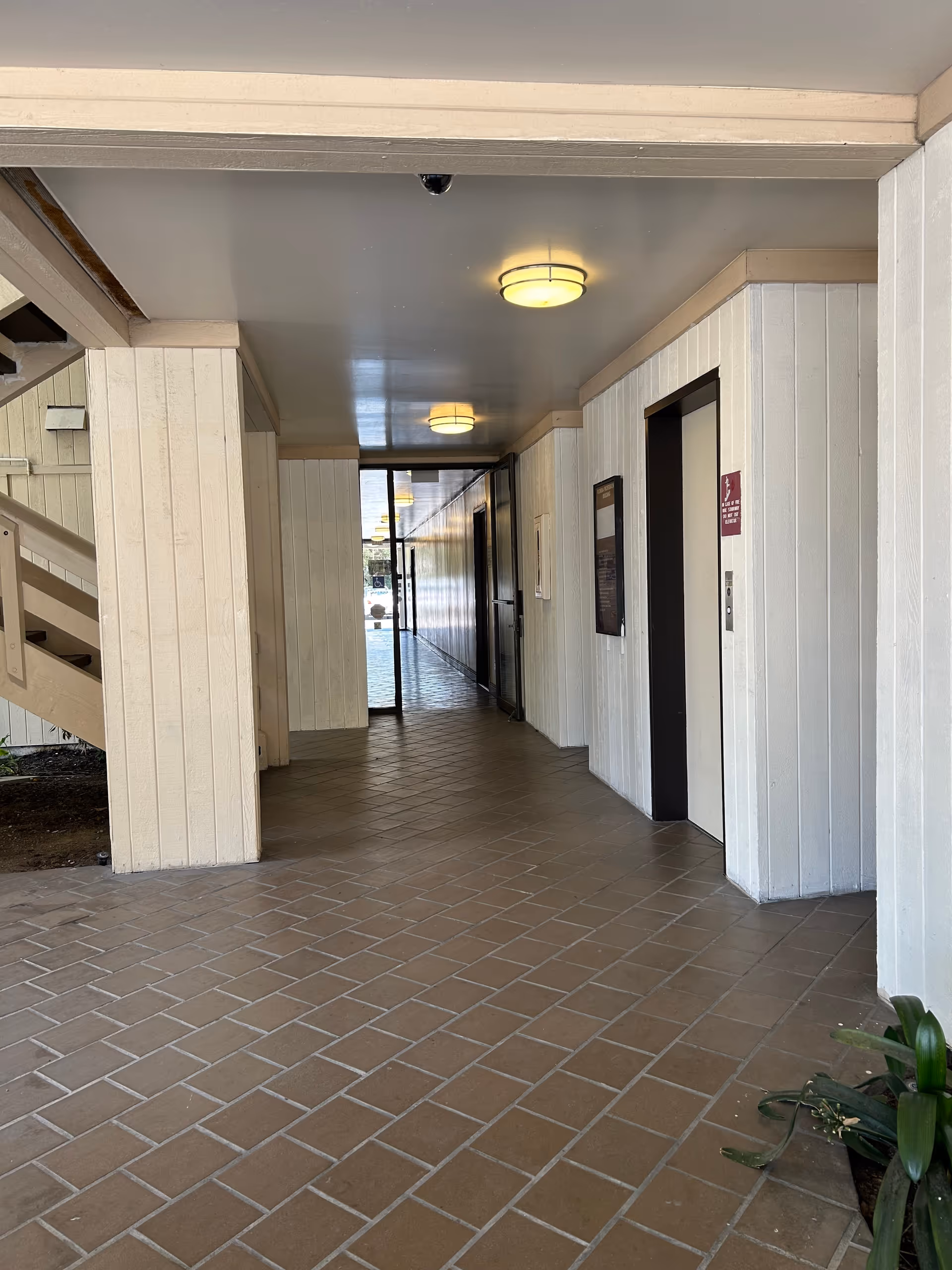 Narrow interior hallway of a senior living facility with tile floor, ceiling lights, and doors.