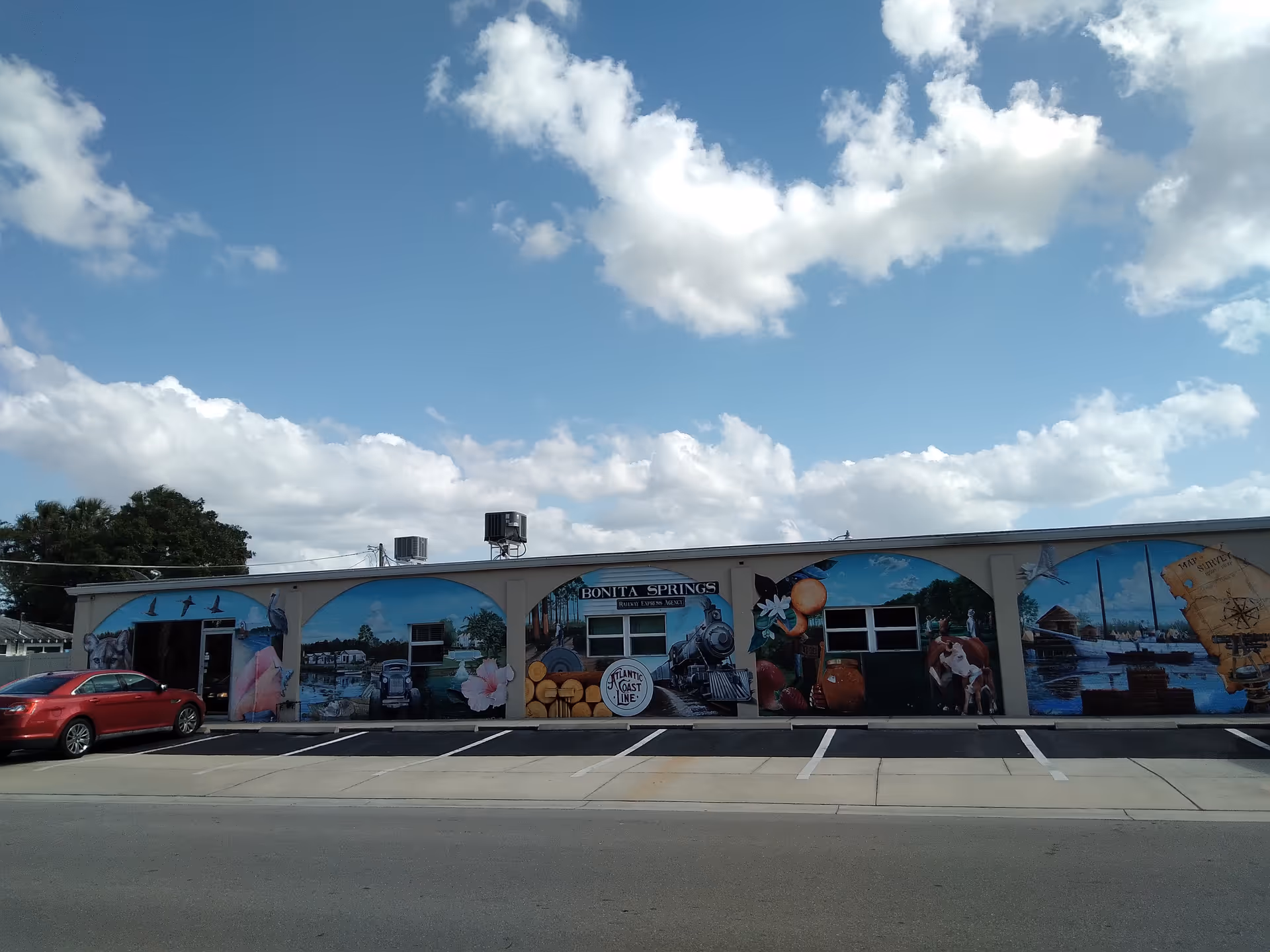 Long, single-story building with colorful exterior murals and a front parking lot.