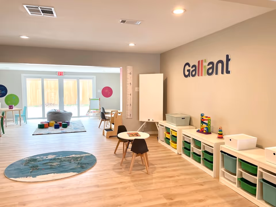 Bright therapy room with toys, small tables, cubbies, and a wall growth chart.