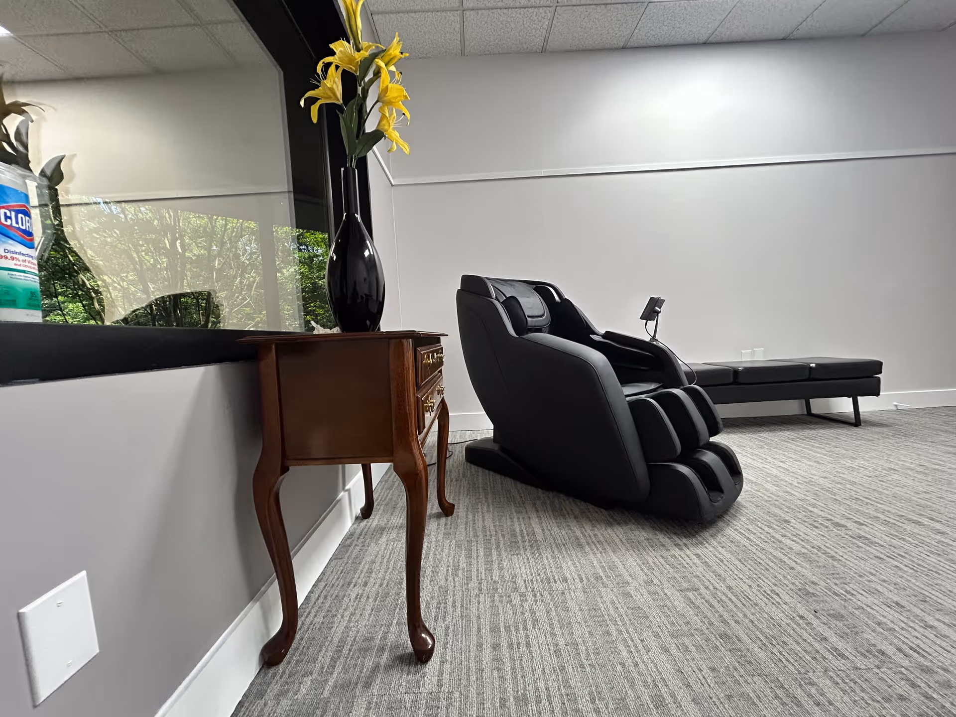 A modern senior living lounge with a black massage chair, console table, and bench.