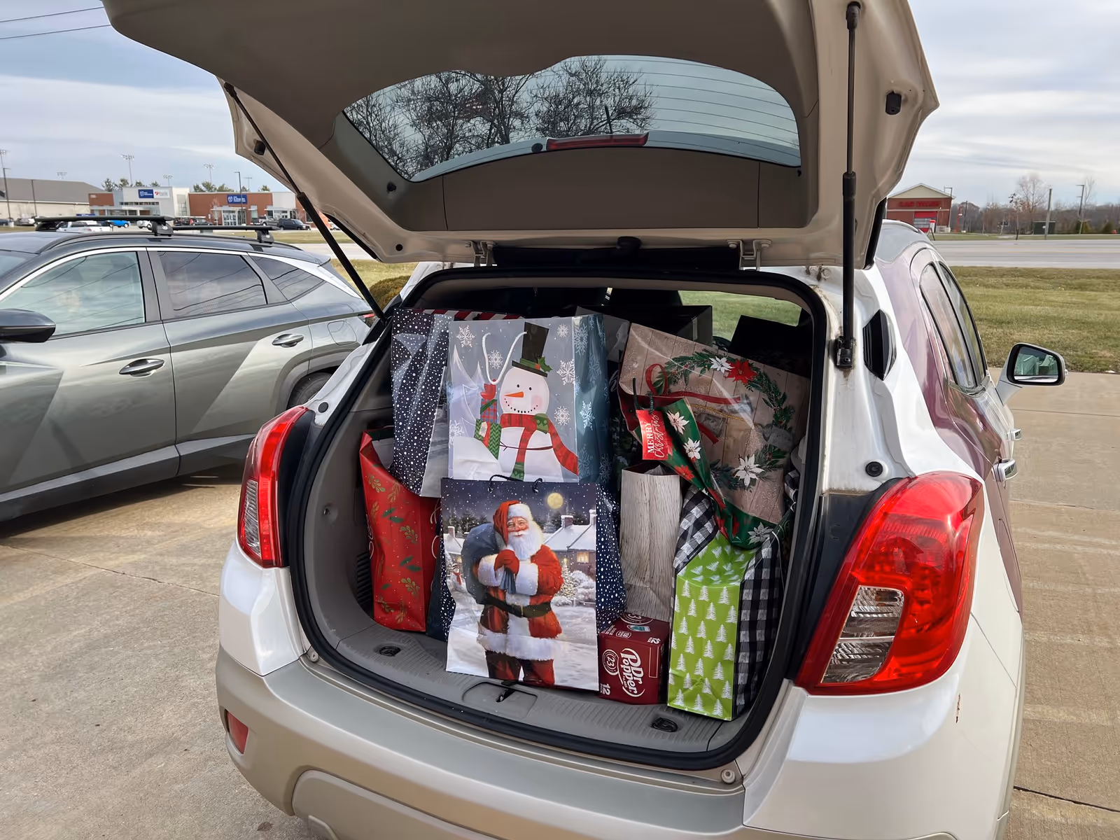 Open trunk of a white SUV filled with Christmas gift bags in a parking lot.
