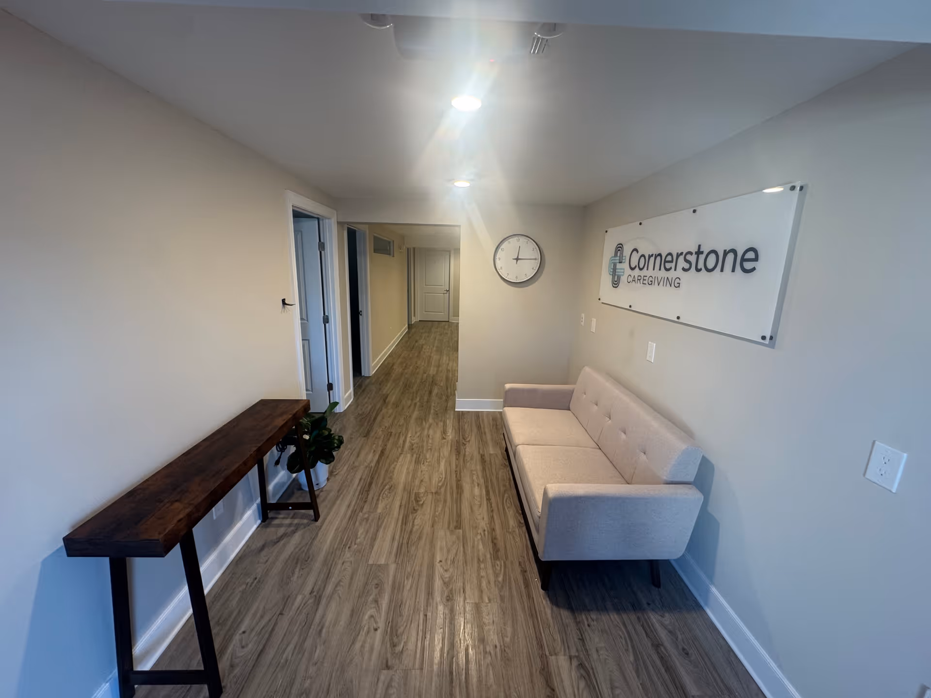 A narrow hallway in Cornerstone Caregiving with a beige sofa, wall clock, and sign.