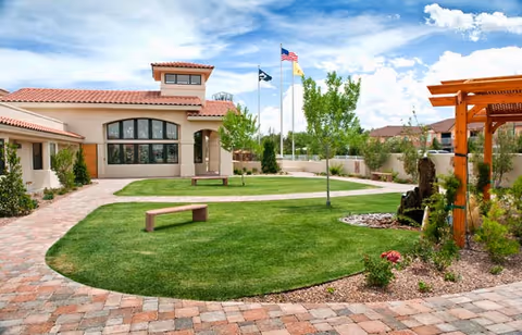 Sunny courtyard with green lawn, benches, flags, and a beige building in the background.