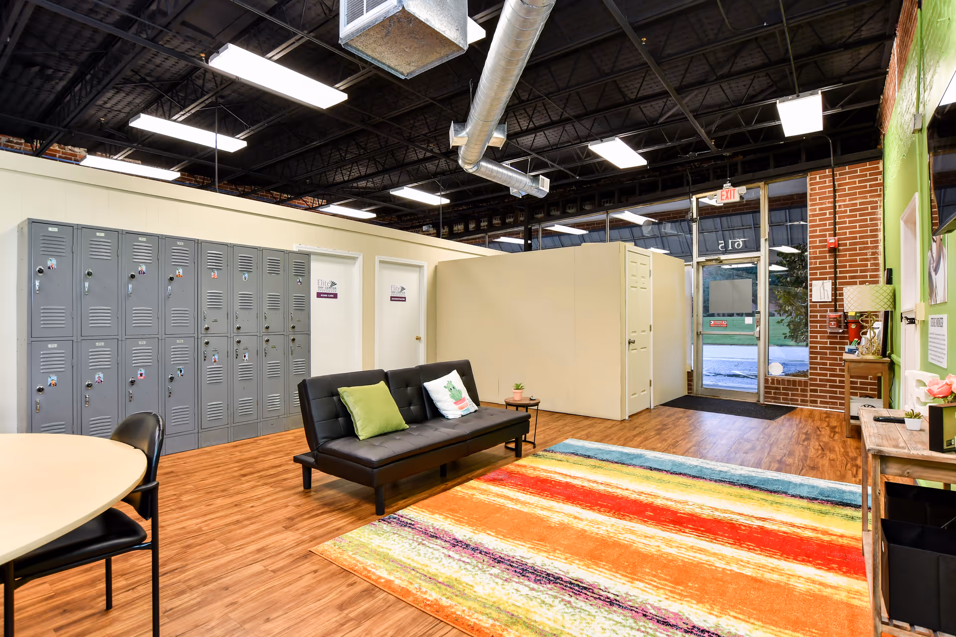 Lounge area inside Elite Home Care and Day Centers with lockers, sofa, and a colorful rug.