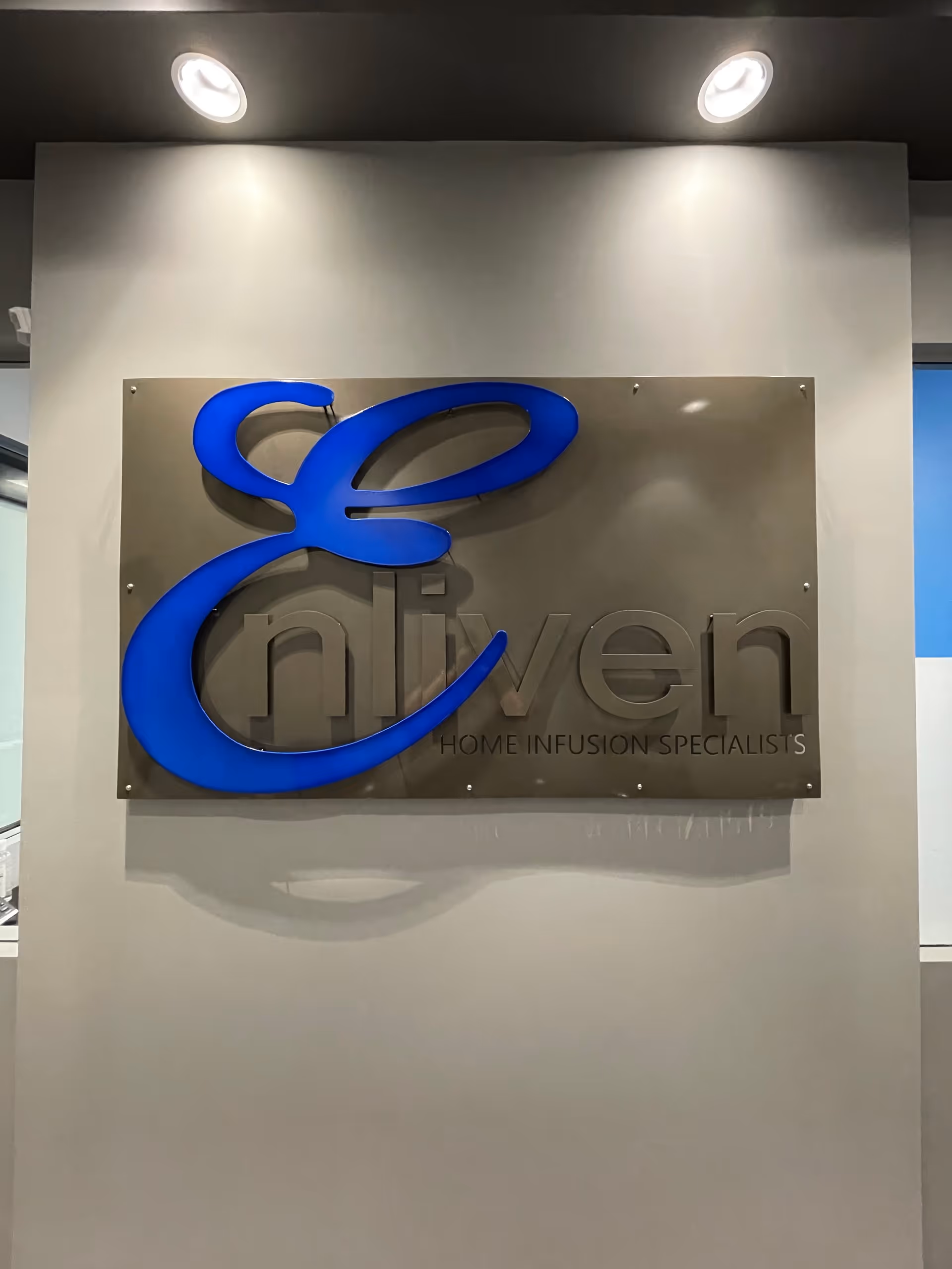 Indoor wall sign displaying the blue Enliven logo and Home Infusion Specialists text.
