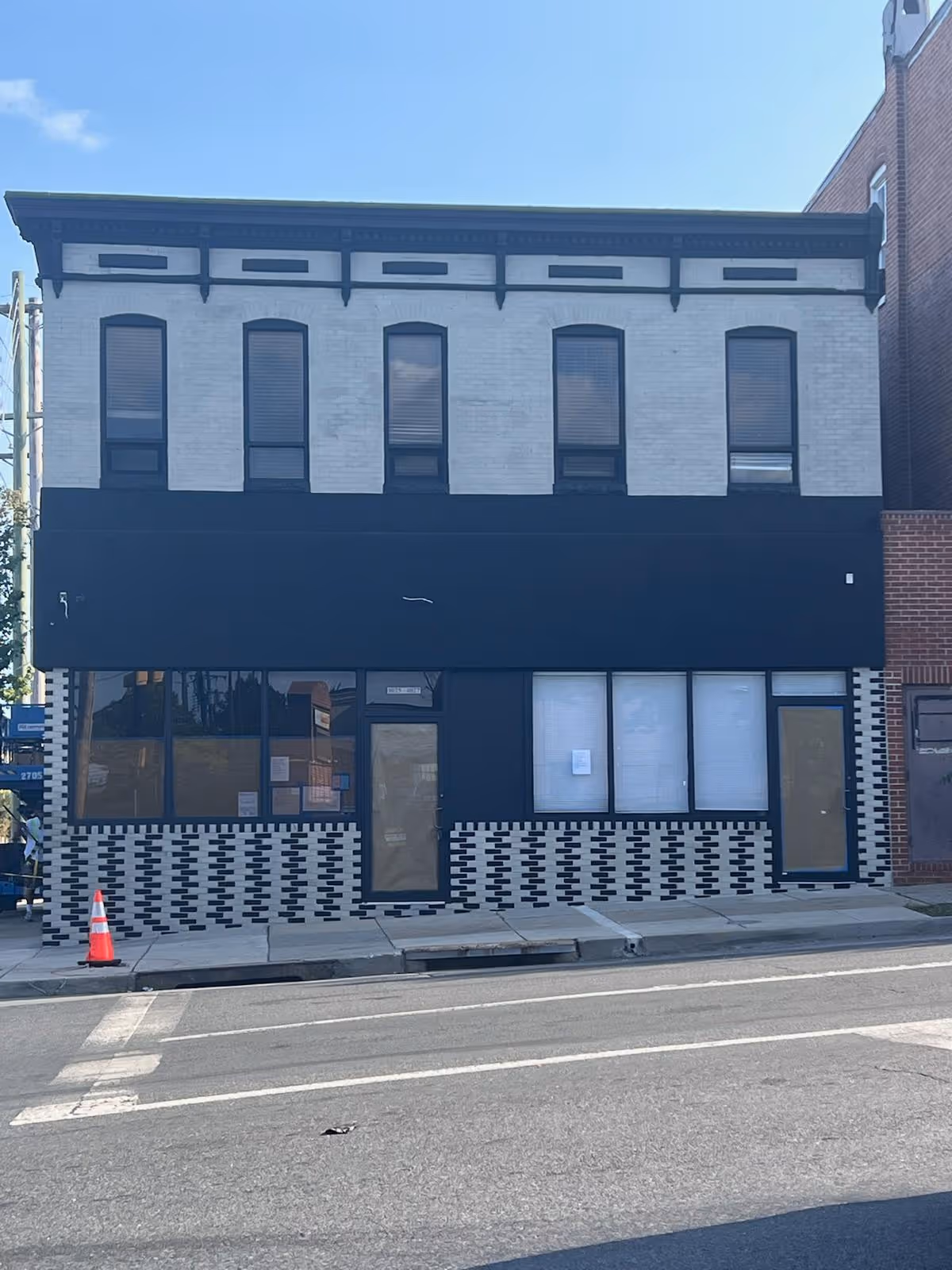 Two-story brick storefront with black facade and large windows along a city street.