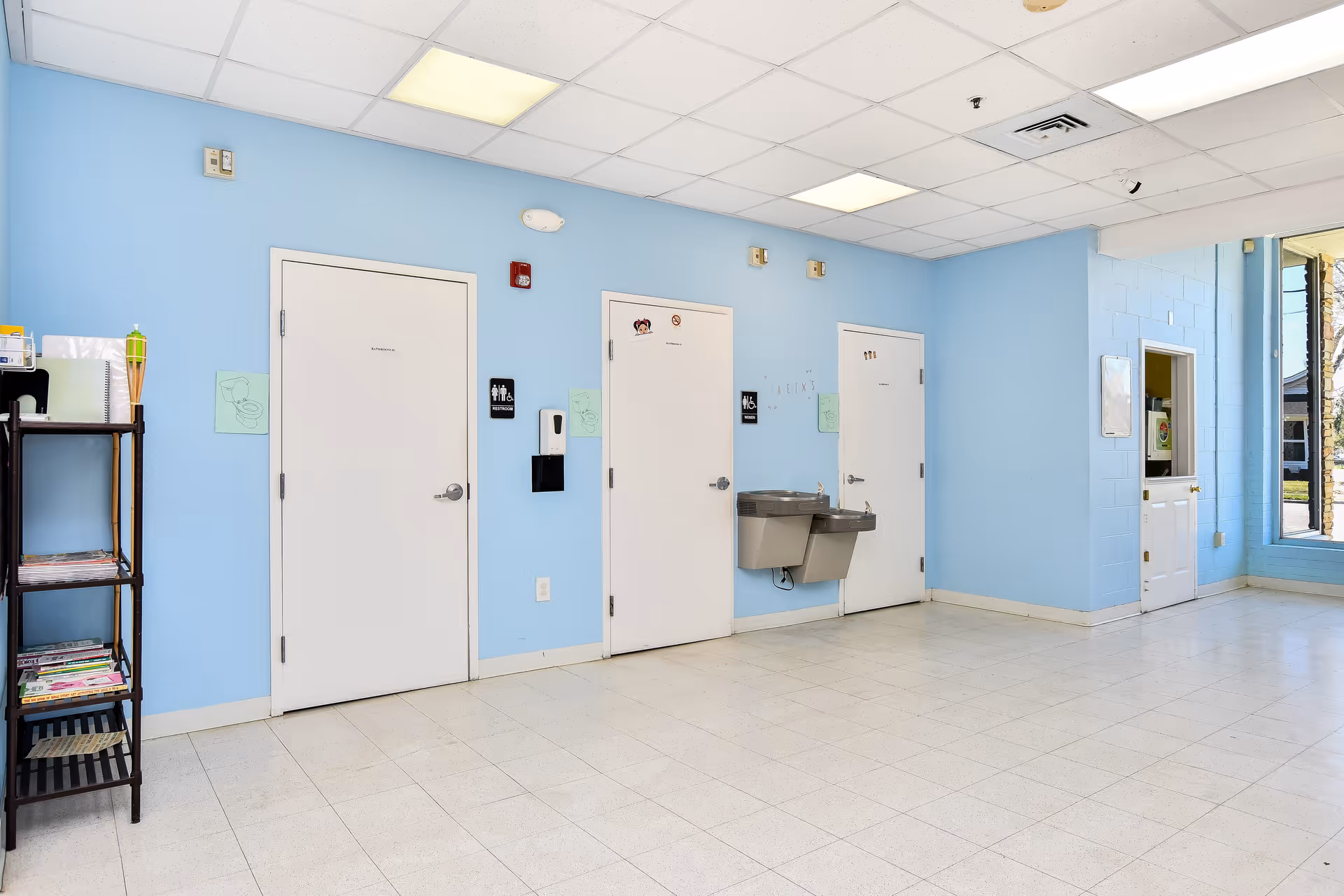 Bright blue hallway interior with several white doors, a sink, shelves, and a window.