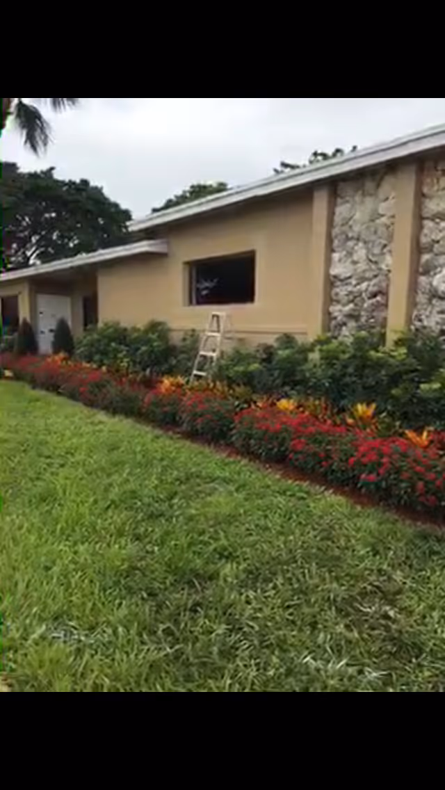 Exterior view of a tan building with stone accents, lawn, and colorful flower beds.